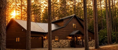 A log cabin with a stone foundation, a metal roof, and a gravel driveway.