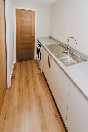 Cocina compacta con lavadora, lavamanos y suelo de madera.