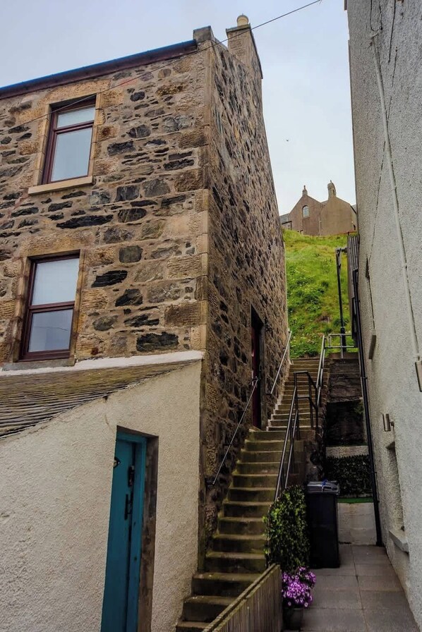 Una calle estrecha con un edificio de piedra, una escalera y una vista distante de una colina.