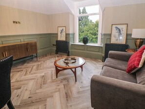 A room with a herringbone floor, a sofa, a chair, a table, and two framed wall art pieces. - The Loft Suite (Buxton)