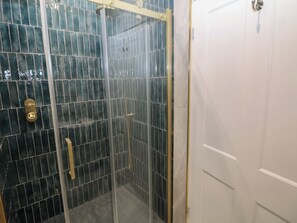 A glass-enclosed shower with a tiled wall, a door with a handle, and a white door to the right. - The Loft Suite (Buxton)