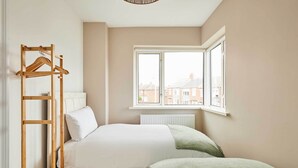 Ein Schlafzimmer mit einem Bett, einem Holz-Kleiderständer, einem Fenster und einer Heizung.