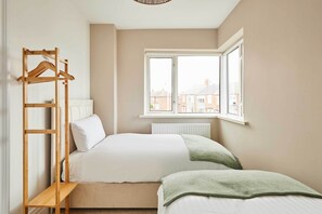 Ein Schlafzimmer mit einem Bett, einem Holz-Kleiderständer, einem Fenster und einer Heizung.