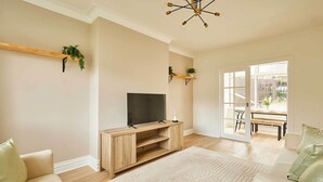Ein Wohnzimmer mit Fernseher auf einem Holzschrank, einer Couch, einem gemusterten Teppich und einer Tür, die nach draußen führt.