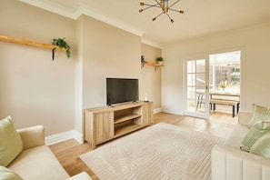 Un salon avec un téléviseur posé sur un meuble en bois, un canapé, un tapis à motifs et une porte donnant sur l’extérieur.