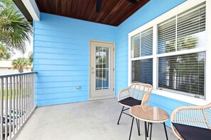 Eine überdachte Veranda mit blauer Holzverkleidung, einer Tür und zwei Korbstühlen mit Kissen.