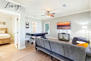 Une pièce comprenant un lit, un canapé gris, une table de massage, un ventilateur de plafond et un tableau.