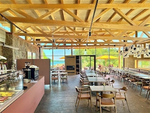 A spacious restaurant with a high ceiling, wooden beams, and large windows offering a view of greenery. - SEEZIEGE Ferienwohungen in der Uckermark (Boitzenburger Land)