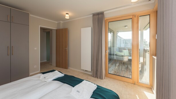 A bedroom with a bed, a wardrobe, a sliding glass door to a balcony, and a white cabinet. - SEEZIEGE Ferienwohungen in der Uckermark (Boitzenburger Land)