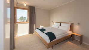 A bedroom with a wooden bed, a nightstand, a window with curtains, and a view of trees. - SEEZIEGE Ferienwohungen in der Uckermark (Boitzenburger Land)