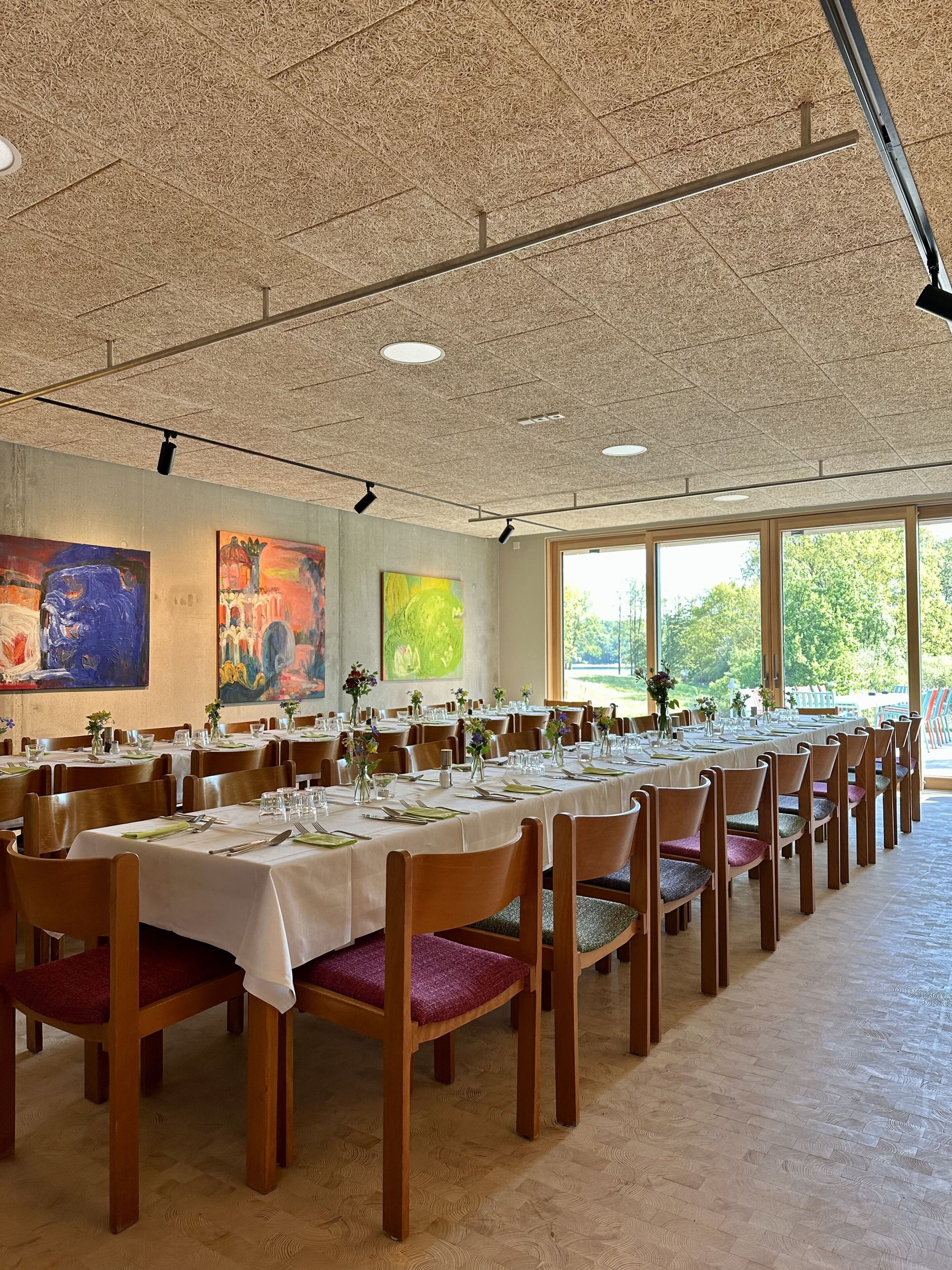 A spacious dining area with long tables, chairs, and artwork on the walls.