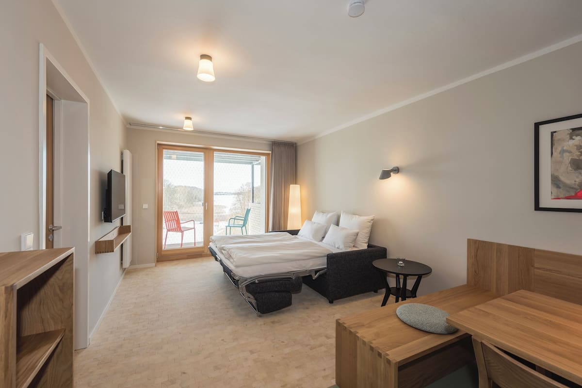 Una habitación de hotel moderna con cama, escritorio, silla, televisor y vistas al exterior.