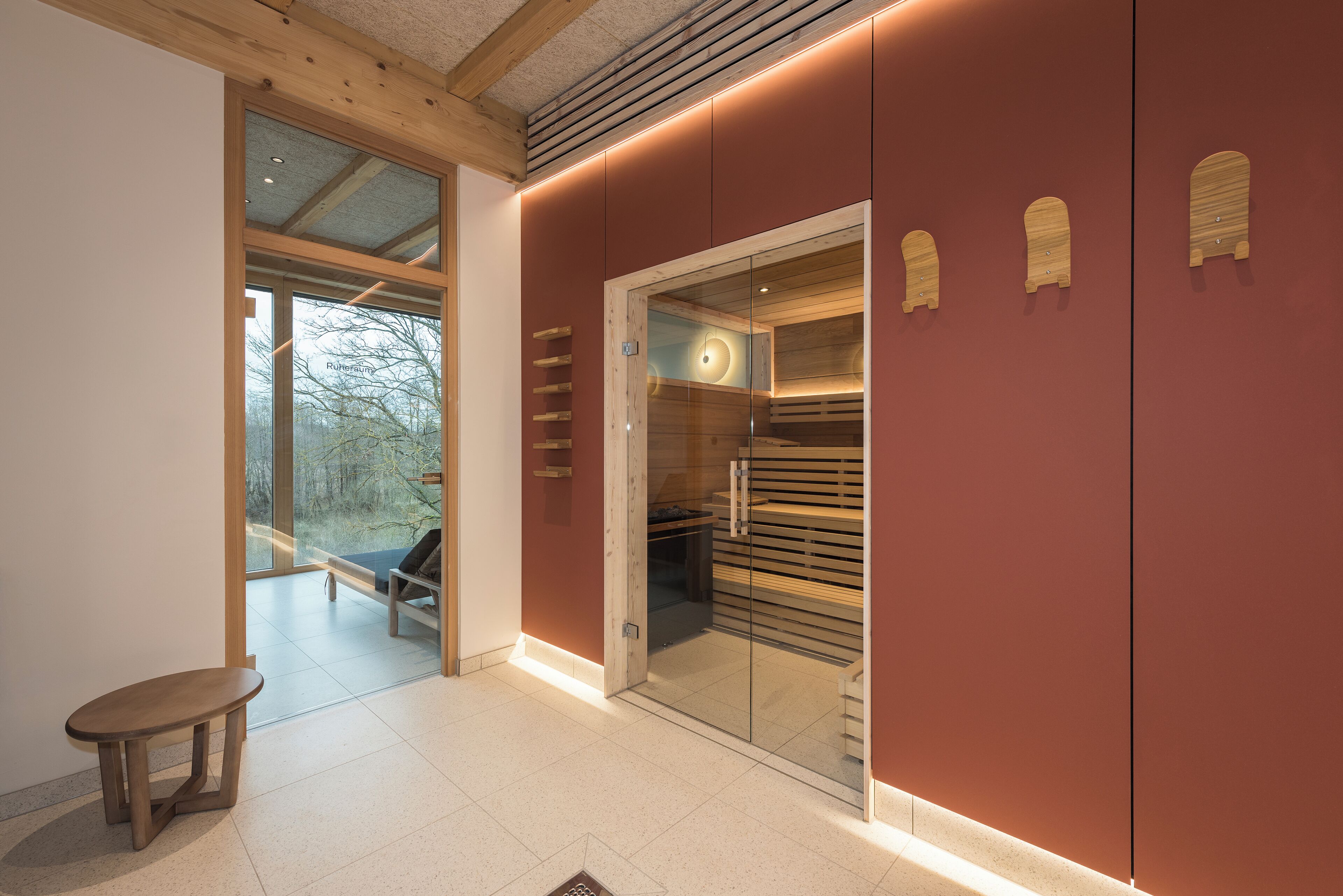 Un interior moderno con un banco de madera, un vidrio que da a una zona de estar y una pared roja con detalles de madera.