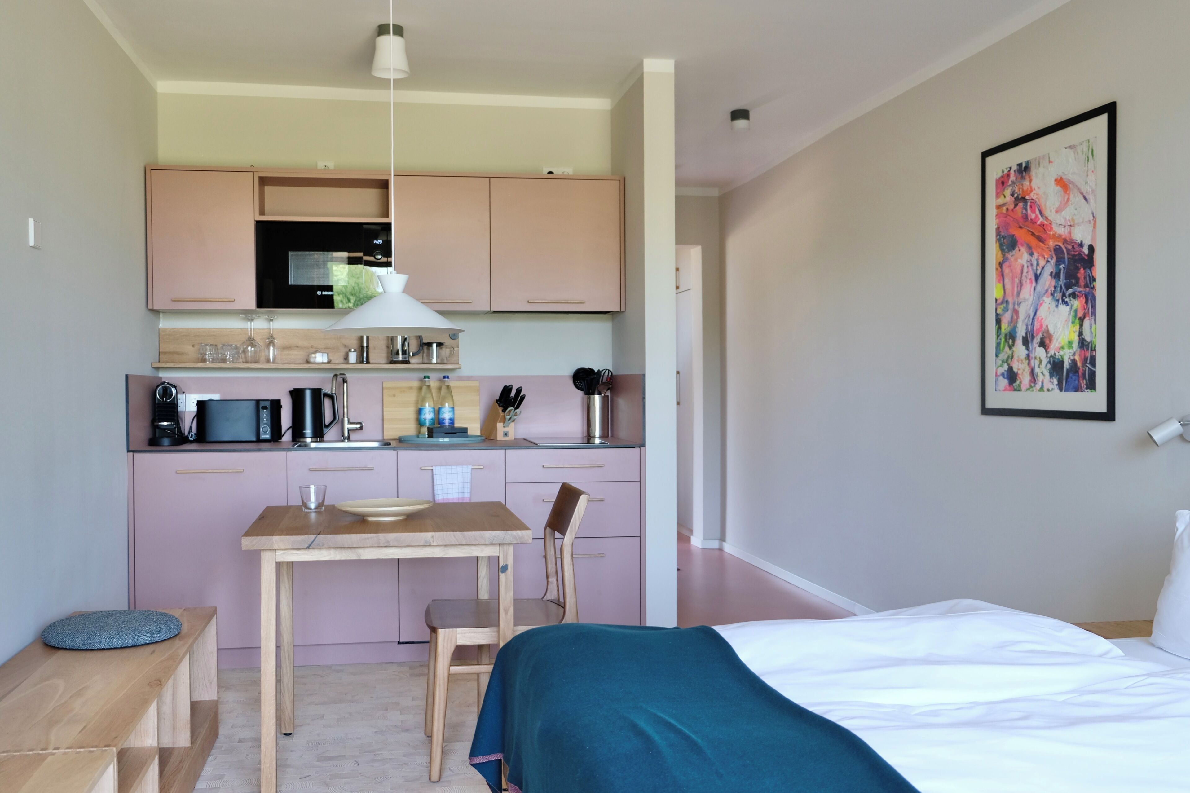 A compact hotel room with a kitchenette, a bed, a dining table, and a chair.