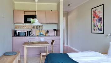 A compact hotel room with a kitchenette, a bed, a dining table, and a chair.
