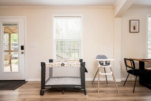 Een kamer met een box, een kinderstoel, een eettafel en een deur naar buiten.
