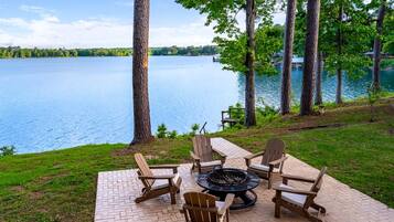 A patio with Adirondack chairs and a fire pit overlooking a lake.