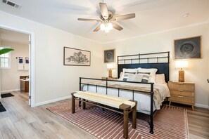 Een slaapkamer met een bed, nachtkastjes, een plafondventilator en kunst aan de wanden.