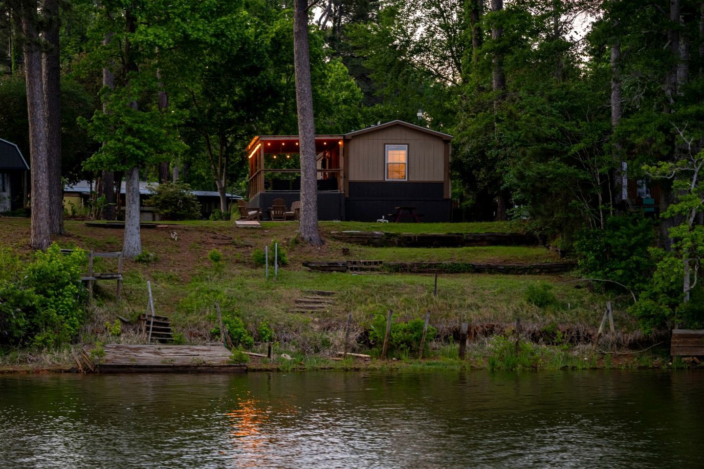 A cabin with a deck, surrounded by trees and a body of water.