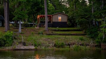 A cabin with a deck, surrounded by trees and a body of water.