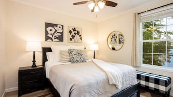 A bedroom with a bed, two bedside tables, a ceiling fan, and a window with a view.