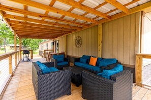 An outdoor covered patio with wicker furniture, a grill, and a wooden deck. - Spacious Modern Cabin on Toledo Bend Lake with Gorgeous Deck and Patio for an Amazing Family Getaway in Hemphill, Texas (Hemphill)