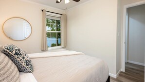 Ein Schlafzimmer mit Bett, Deckenventilator, Fenster mit Vorhängen, rundem Spiegel und Tür.