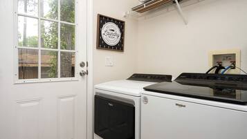 A laundry room with a Whirlpool washer and dryer, a window, and a sign indicating it's a self-service room open 24 hours.