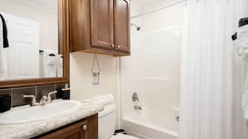 A bathroom with a double sink, a toilet, a bathtub, and a shower curtain.