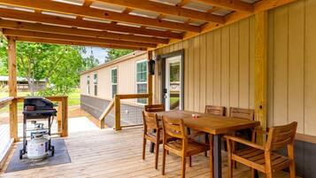 A covered outdoor patio with a wooden table and chairs, a grill, and a propane tank.