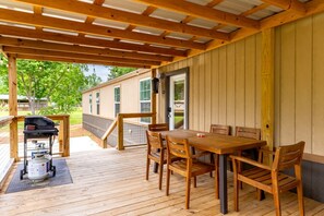 A covered outdoor patio with a wooden table and chairs, a grill, and a propane tank. - Spacious Modern Cabin on Toledo Bend Lake with Gorgeous Deck and Patio for an Amazing Family Getaway in Hemphill, Texas (Hemphill)