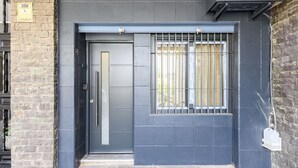 A building entrance with a dark grey door, a barred window, and a stone wall on the left. - (MDV120) Study in Carabanchel, Madrid (Madrid)