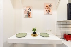 Een wit aanrecht met twee groene borden, een kleine potplant en twee abstracte kunstwerken aan de muur.