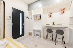 Een moderne kamer met een bed, een bureau met twee stoelen, een klein tafeltje, een zwarte deur en een witte muur met een stopcontact.
