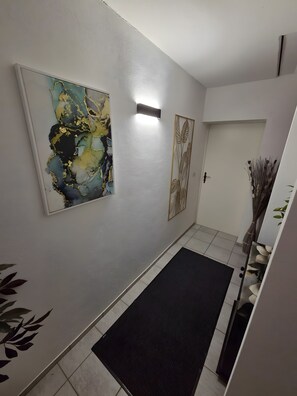 Un pasillo con un tapete negro, una lámpara de pared y dos cuadros enmarcados.