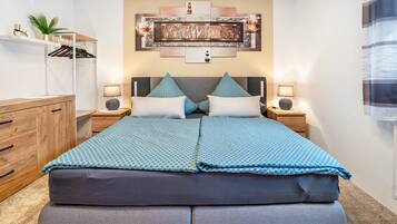 Una cama doble con una colcha estampada, dos mesitas de noche con lámparas, un aparador de madera y una obra de arte colgada en la pared.