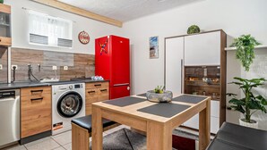 A compact kitchen with a red refrigerator, a washing machine, and a dining area with a wooden table and black mats. - Apartment Kastanie in Selb – Quiet Location Near Nature Reserve, Garden Lounge, Pet Friendly (Selb)