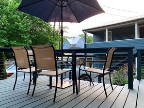 Eine Terrasse mit Gartenmöbeln, darunter Stühle und ein Tisch, sowie ein großer Sonnenschirm, der Schatten spendet.
