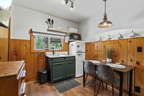 Et kompakt køkken med træskabe, et køleskab, en vask og et spiseområde med bord og stole.
