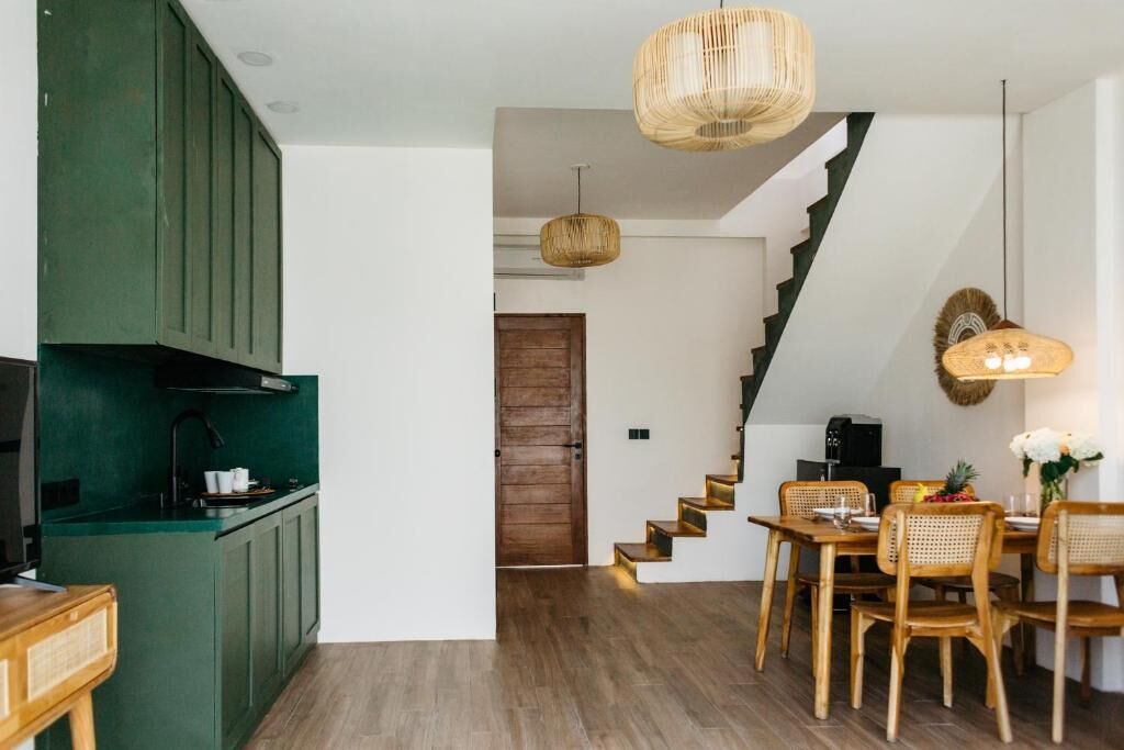 Una cocina moderna con armarios verdes, un comedor con sillas de madera y una escalera que sube a otro nivel.