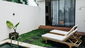 A modern outdoor pool area with a glass-enclosed room, lounge chairs, and a small garden.