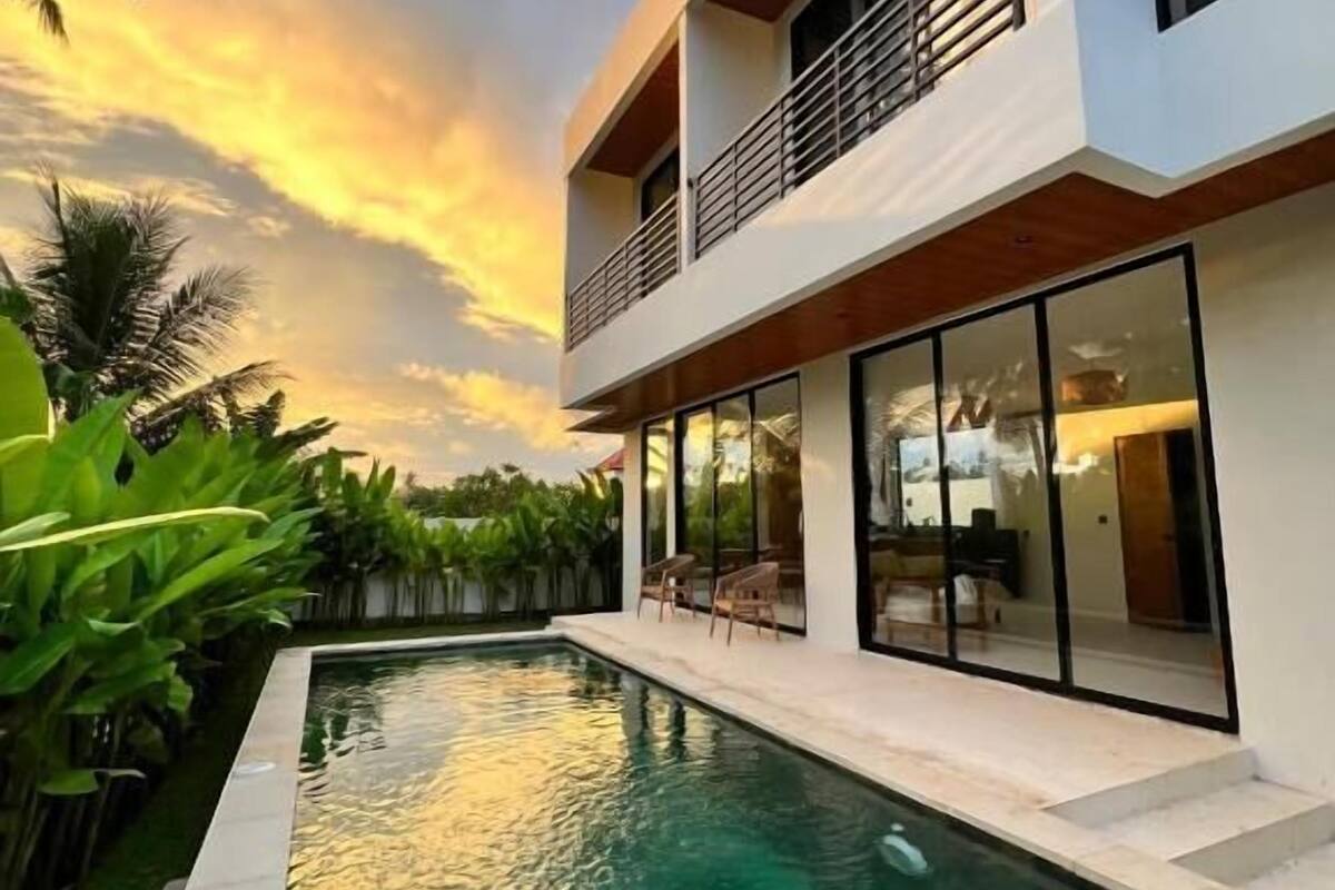 Una casa moderna de dos pisos con piscina, ventanas amplias y un balcón.