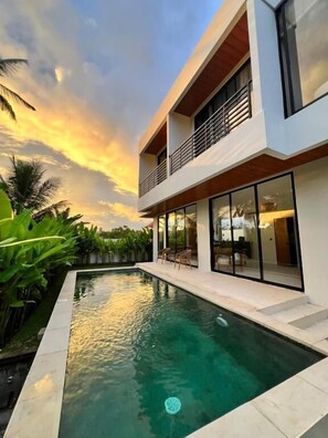 Una casa moderna de dos pisos con piscina, ventanas amplias y balcón.