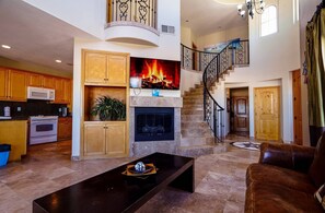 A spacious living area with a fireplace, a kitchen with wooden cabinets, a staircase, and a modern coffee table.