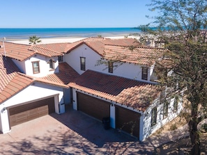 A white building with red-tiled roofs and a garage, overlooking a beach.