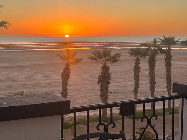 A sunset view from a balcony with palm trees and a beach in the background.