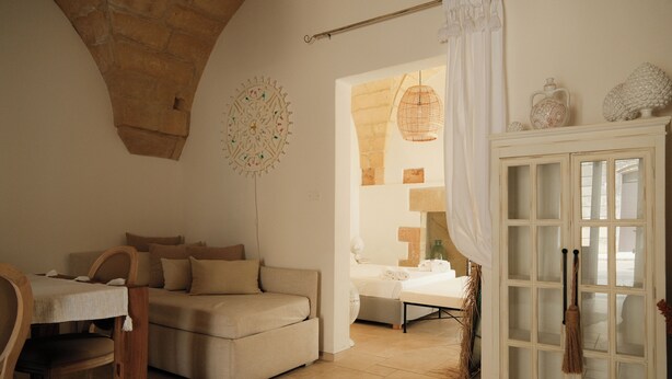 Una habitación con un arco de piedra, una mesa de madera, un sofá, un aparador con puertas de cristal y una lámpara colgante.