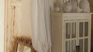 Una habitación con un armario blanco, un espejo y una cortina blanca colgada.
