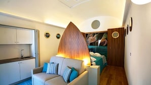 A compact room with a sofa, a bed, a wooden accent wall, a small kitchen area, and a circular ceiling feature. - Grotta Verde Luxury Suite (Capri)