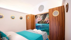 A bedroom with a bed, a wooden wardrobe, and a large painting of a natural scene. - Grotta Verde Luxury Suite (Capri)